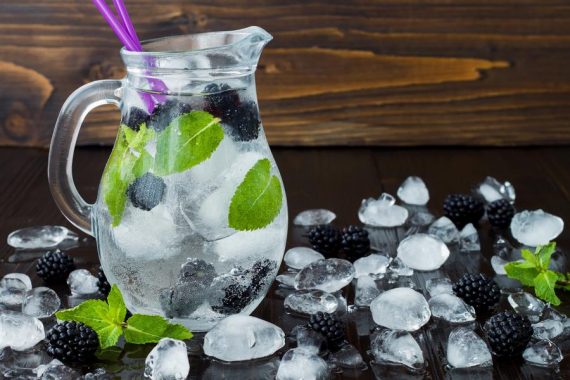 Healthy detox flavored water with blackberry and mint. Cold refreshing berry drink with ice on dark wooden table. Copy space background